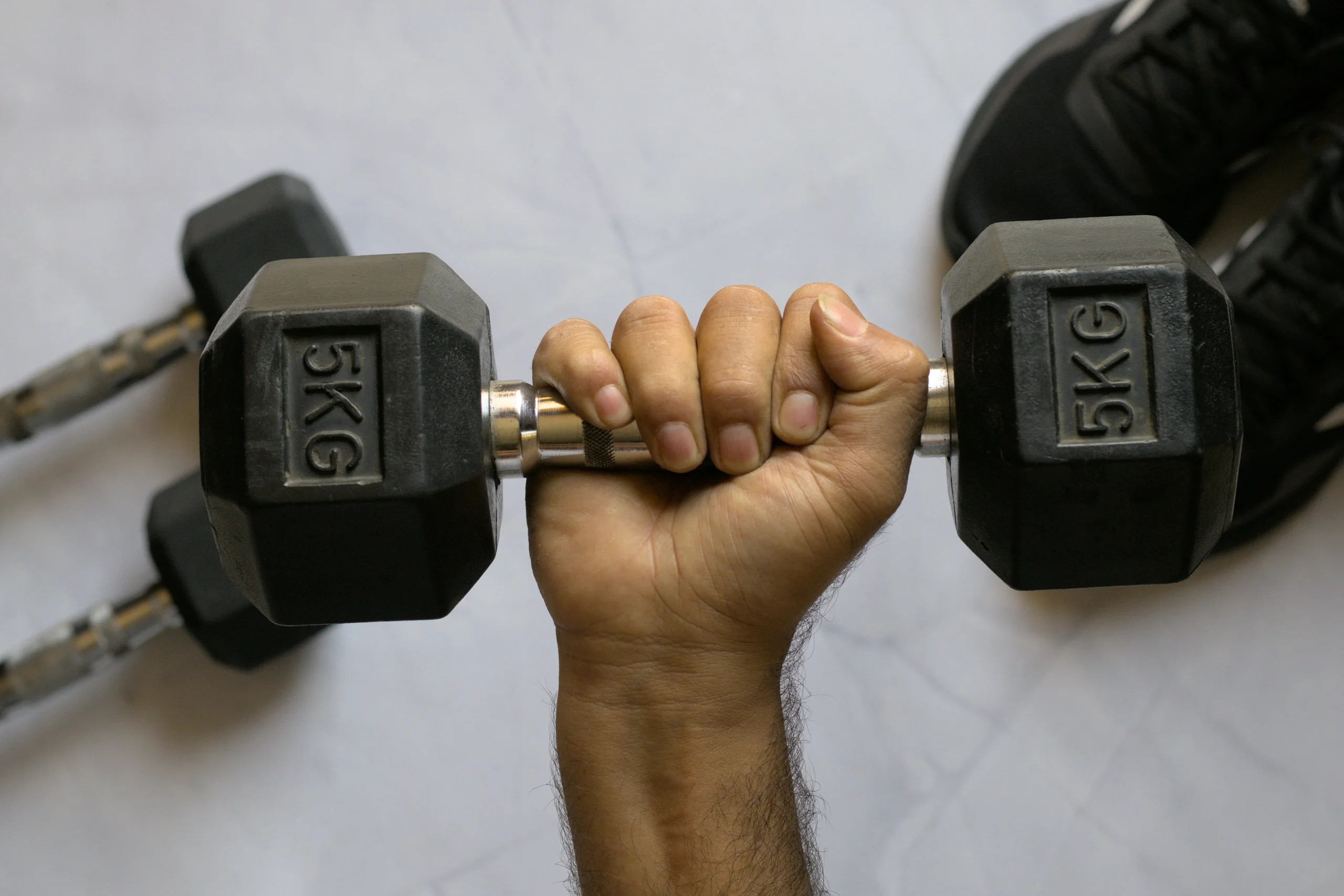 A dumbbell held in a hand over a white granite surface